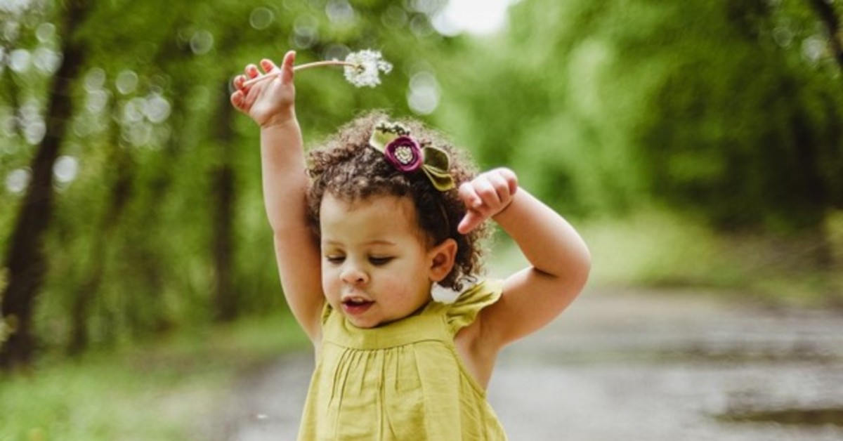 Toddler playing outside with dandelion in hand