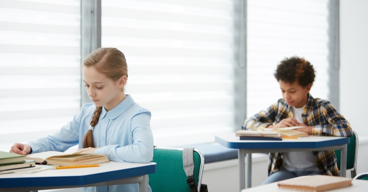 Male and female student sitting in a classroom, reading books at their desks.