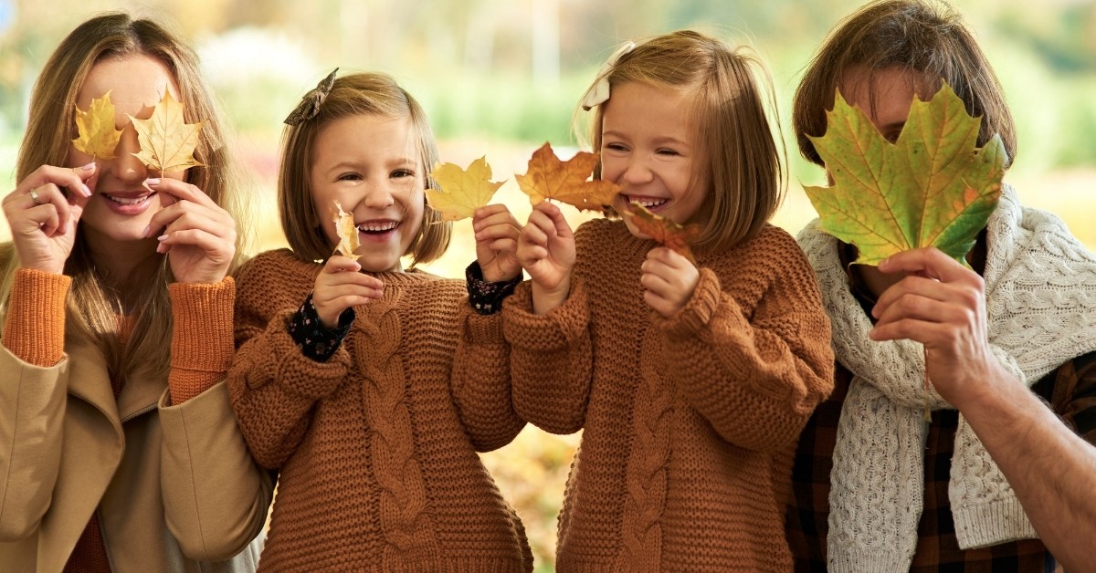 Parents with two daughters holding fall leaves over their faces