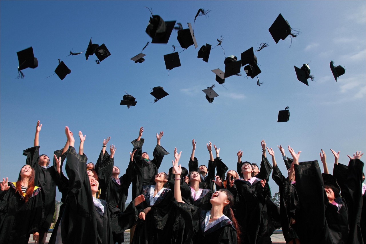 Students in black robes tossing graduation caps into the blue sky.